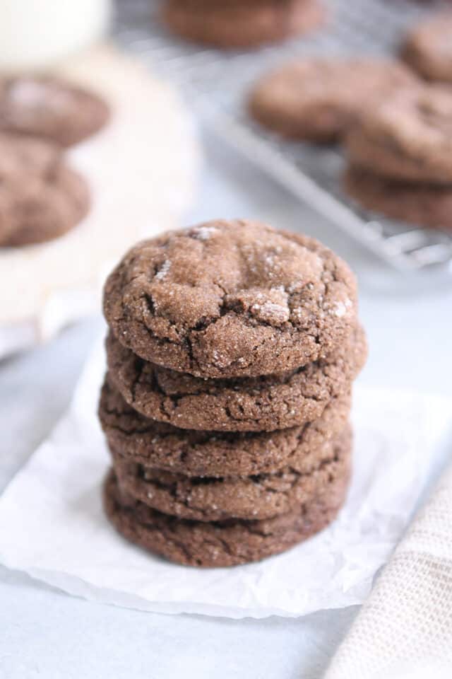 Stack of five chewy chocolate ginger molasses cookies on white parchment paper.