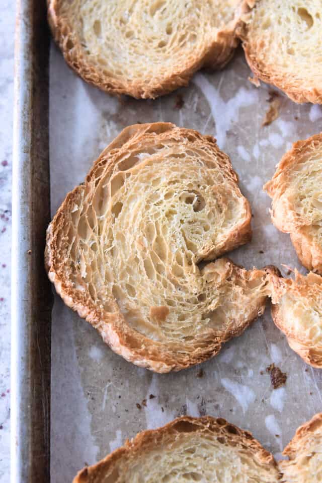 Halved croissants toasted on parchment lined baking sheet.