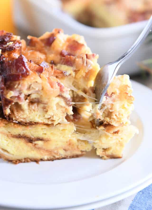 Cheese strings pulling as fork takes bite from breakfast casserole on white plate.