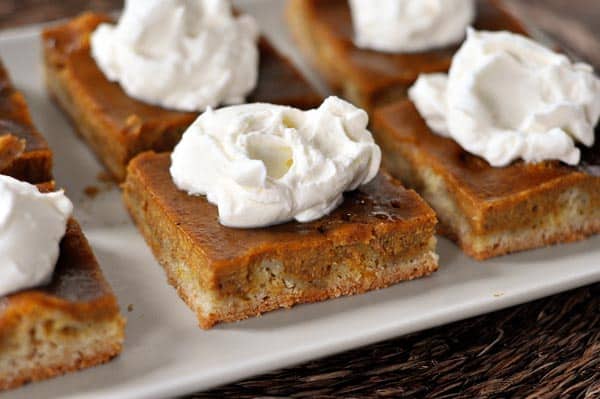 pieces of pumpkin pie sheet cake with whipped topping on top on a white platter