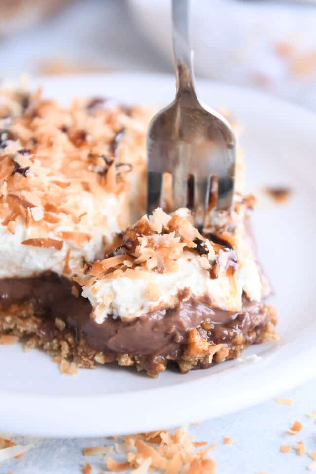 Fork scooping bite of dessert with coconut crust, chocolate pudding, whipped cream and toasted coconut.