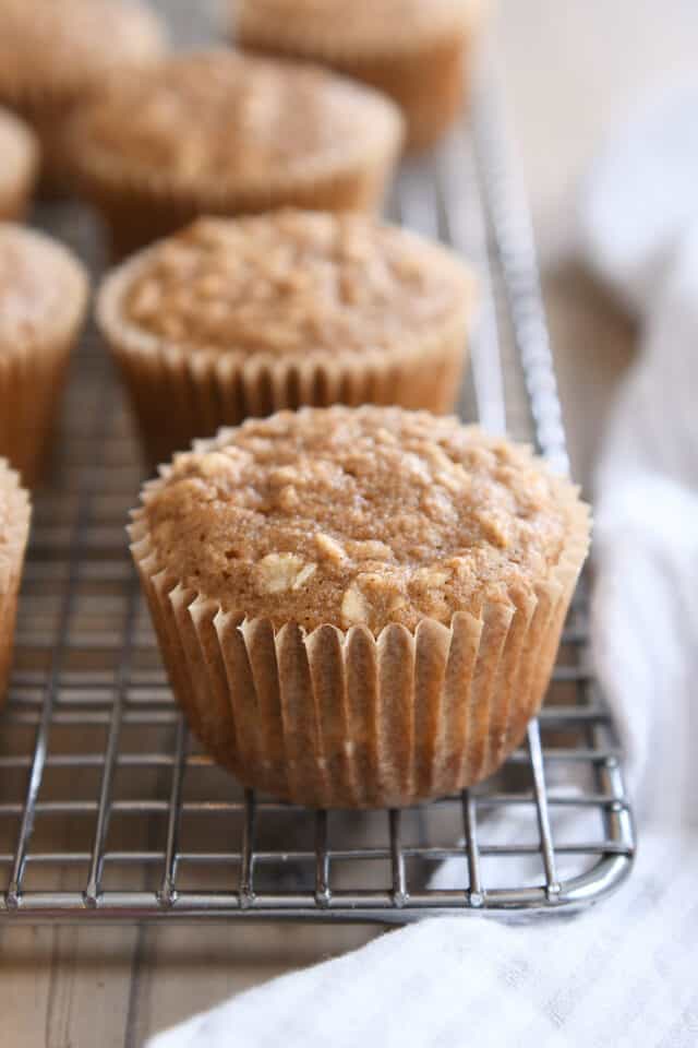 Applesauce oat muffin in paper wrapper on wire rack.