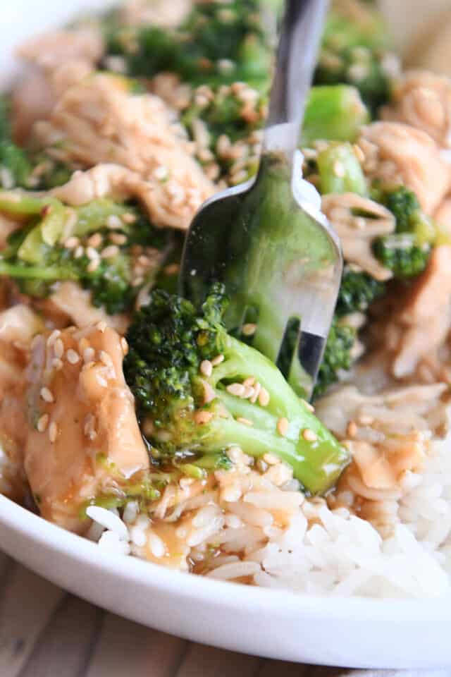 White bowl with rice, broccoli, chicken, sesame seeds and fork.