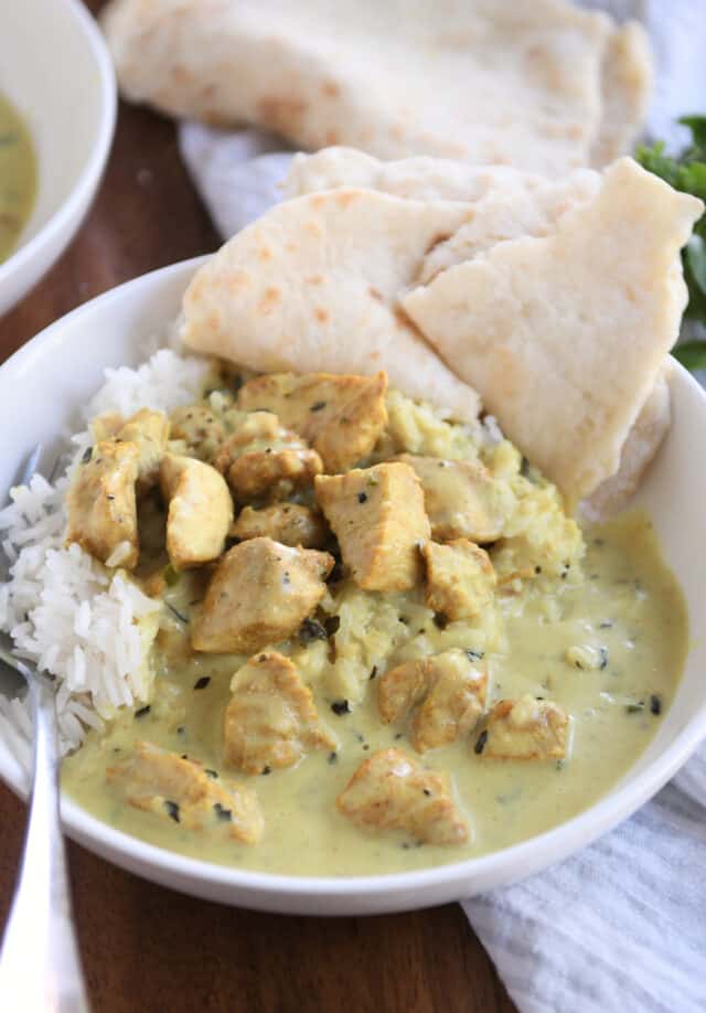White bowl with rice, fork, chicken pieces, coconut curry sauce, naan.