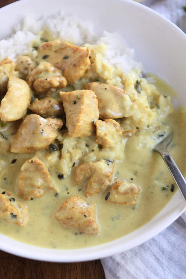 Close up of chicken pieces, coconut curry sauce, and rice in white bowl.
