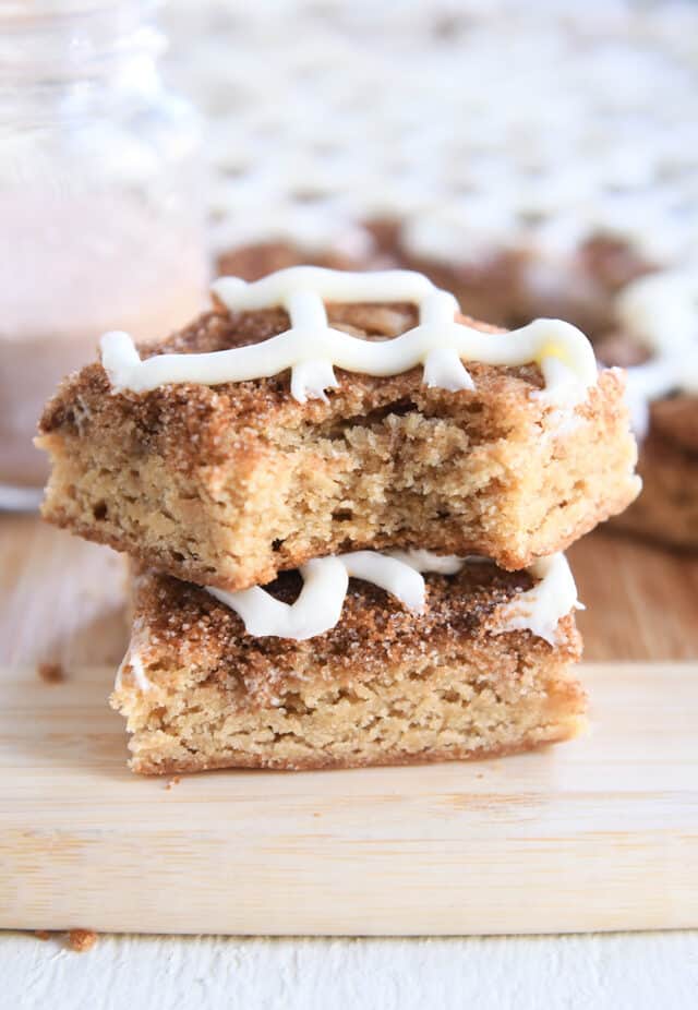 Two cinnamon roll blondie bars stacked on each other on wood cutting board.