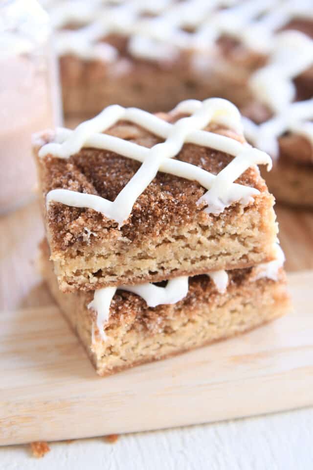 Two cinnamon roll blondies stacked on each other on wood cutting board.