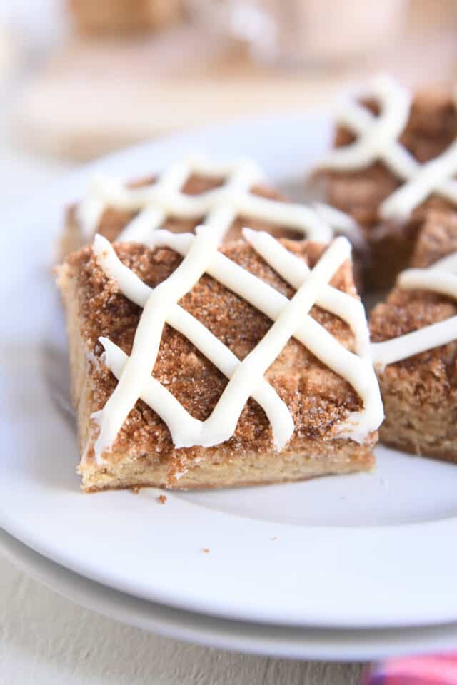 Cinnamon roll blondie bar with cream cheese frosting swirl on white plate.