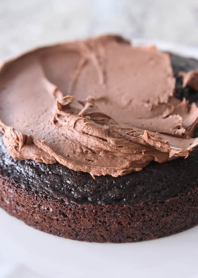 spreading chocolate frosting on top of one round of chocolate cake