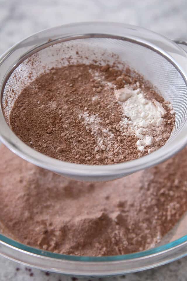 Sifting cocoa powder, flour and sugar in mesh strainer into glass bowl.