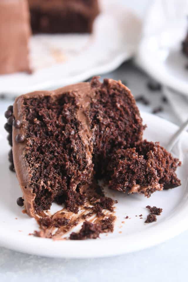 Piece of chocolate cake with chocolate frosting on white plate with fork.