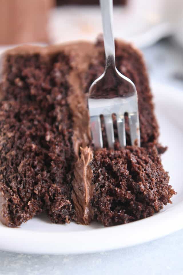 Fork taking piece of chocolate cake on white plate.