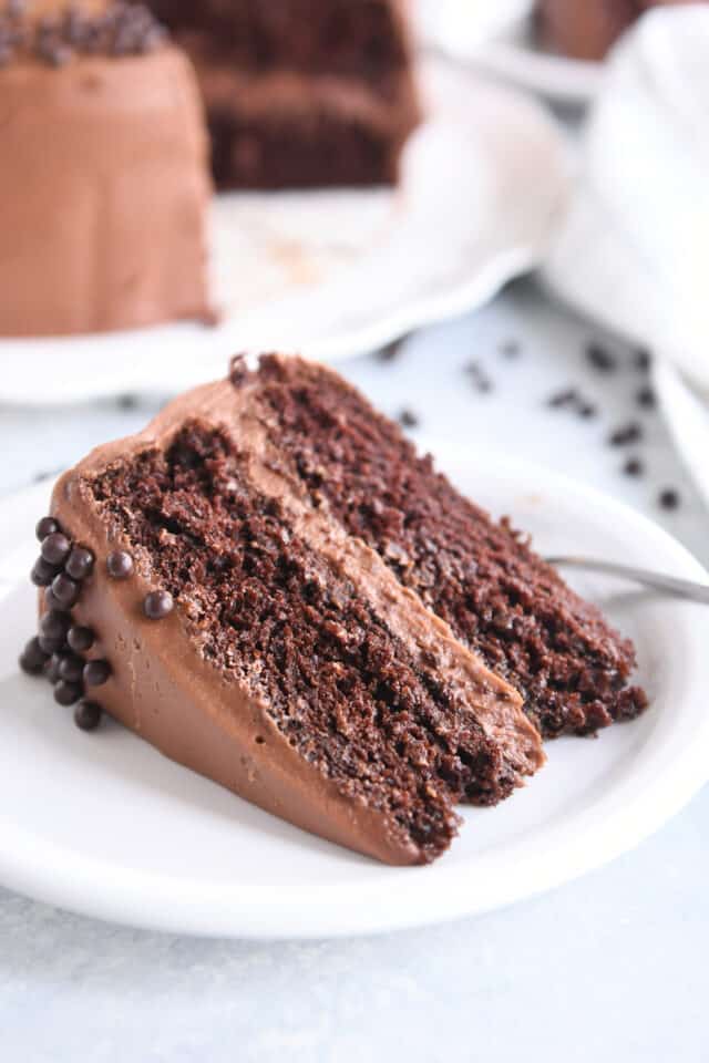 Piece of chocolate cake with chocolate frosting on white plate with chocolate pearls.