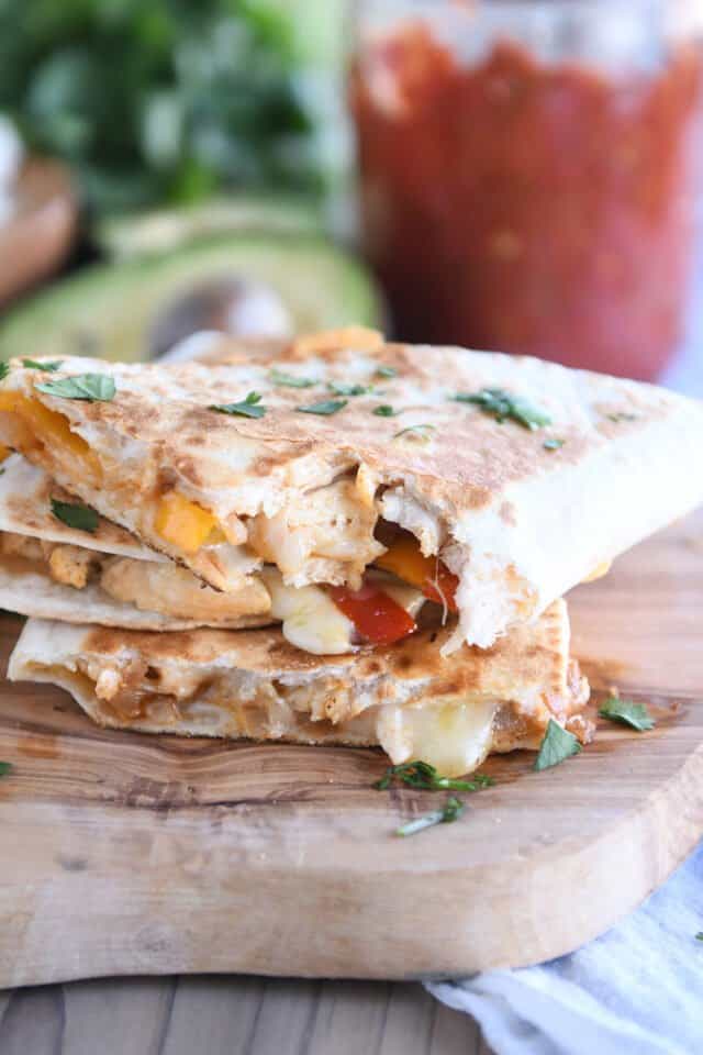 Three triangle quesadillas stacked on wooden board.