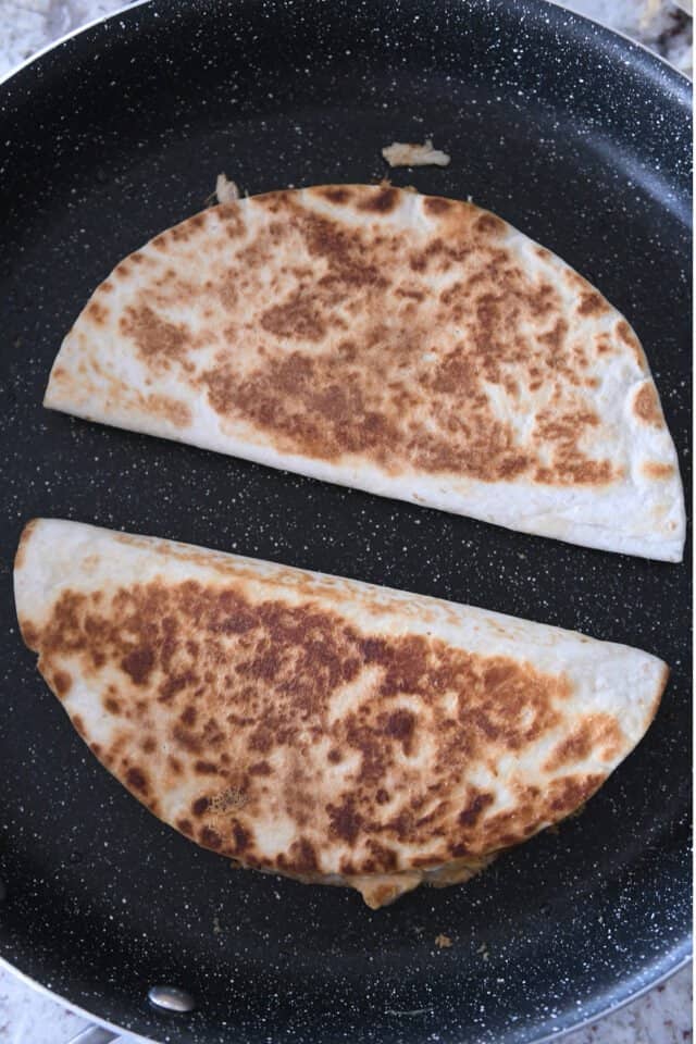 Two folded quesadillas cooking in skillet.