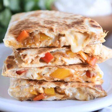 four chicken quesadilla triangles stacked on white plate