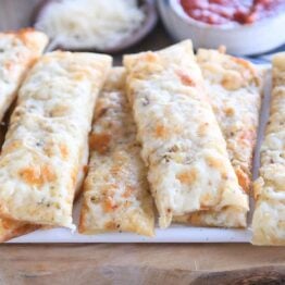 eight cheesy breadsticks on wood cutting board