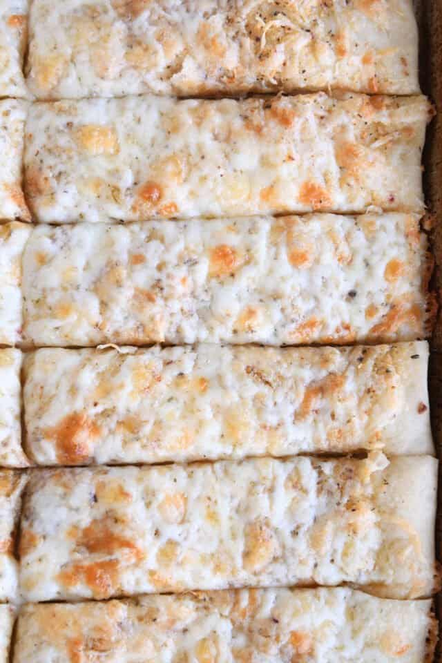 Close up view of six cheesy breadsticks on sheet pan.