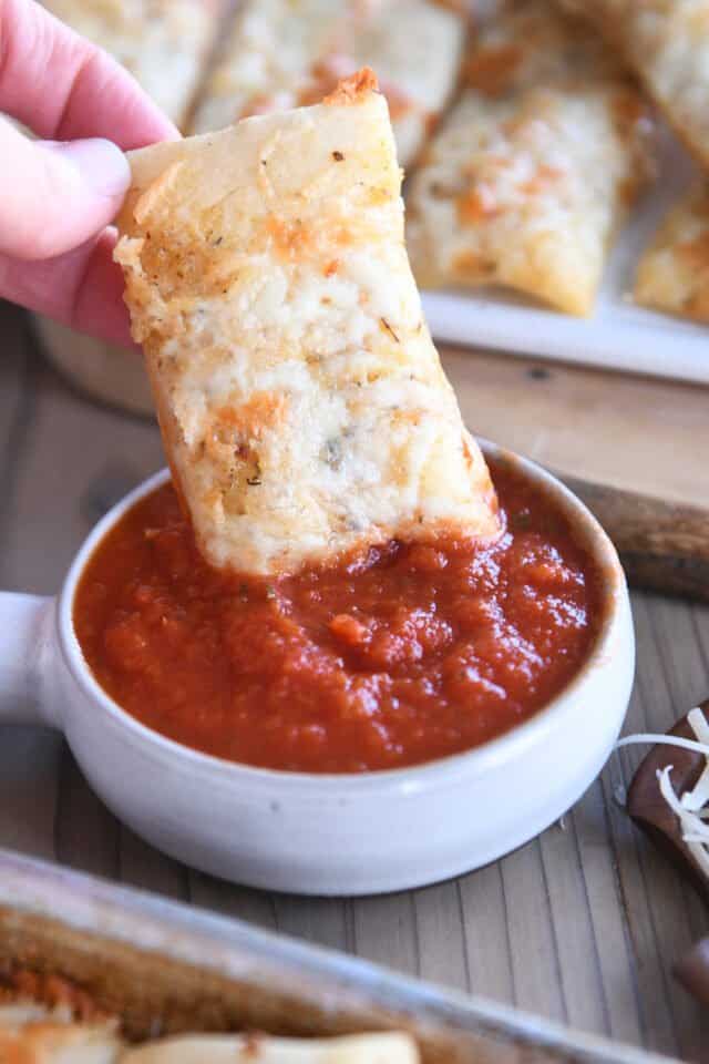 Dipping cheesy breadstick into marinara sauce.