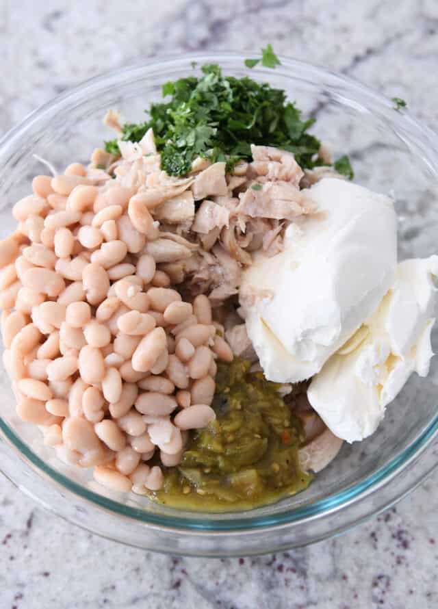 Glass bowl with white beans, green chiles, cream cheese, chicken, cilantro.