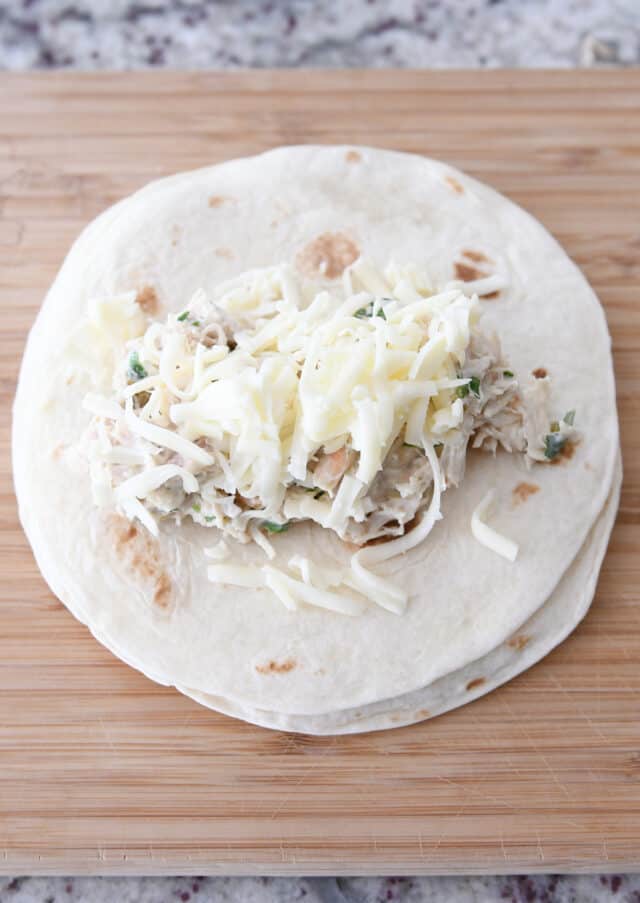 8-inch tortilla with enchilada filing and cheese on wood cutting board.