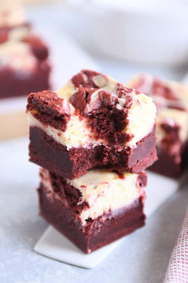 two red velvet cheesecake brownies stacked with bite taken out of the top brownie