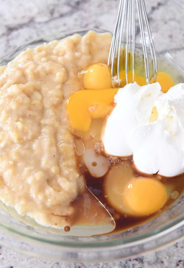 A glass bowl of sour cream banana bread ingredients getting mixed together. 