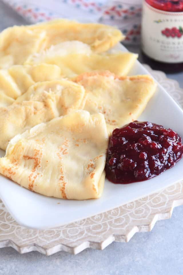 Seven folded Swedish pancakes on white tray with lingonberry jam.
