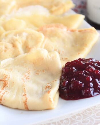seven folded Swedish pancakes on white tray with jam