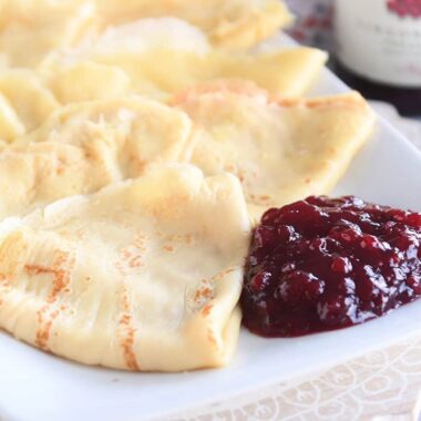 seven folded Swedish pancakes on white tray with jam
