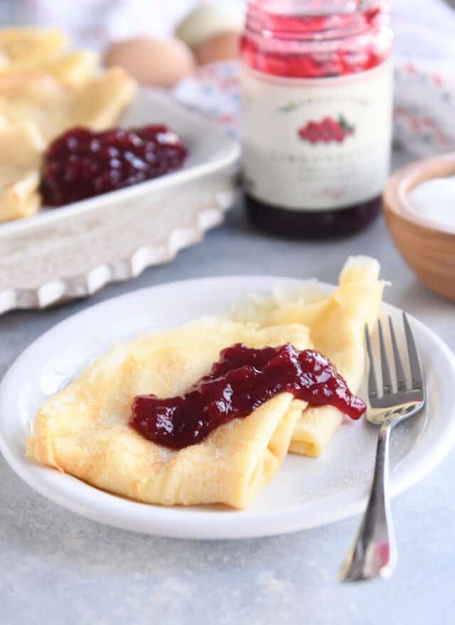 Two triangle Swedish pancakes on white plate with jam and fork.
