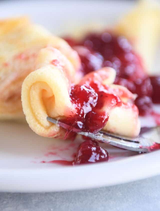 curled up piece of Swedish pancake with lingonberry jam on fork