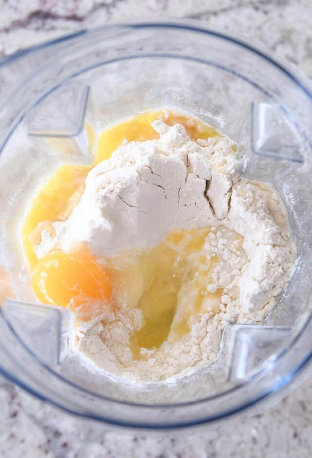 Top down view of blender with flour, eggs, milk, oil.