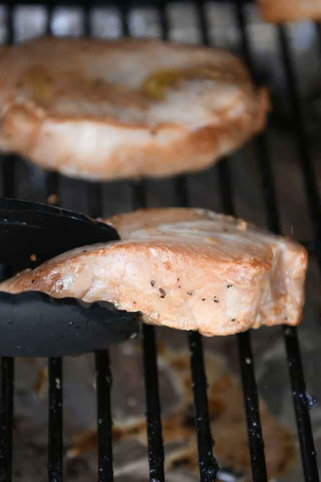 Flipping pork chop with tongs on grill.