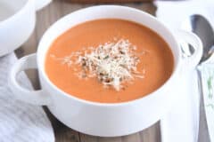 white bowl with handles filled with creamy tomato basil soup with Parmesan for topping