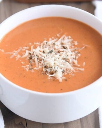 white bowl with handles filled with creamy tomato basil soup with Parmesan for topping