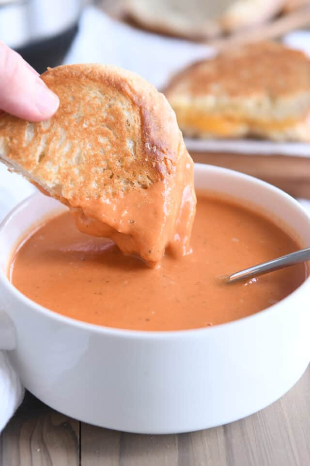 Dipping half of grilled cheese on sourdough bread into bowl of creamy tomato basil soup.