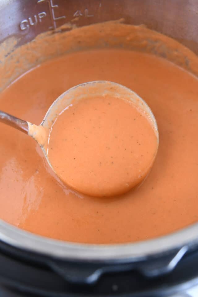 Ladle lifting up scoop of instant pot creamy tomato basil soup.