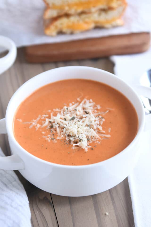 white bowl with handles filled with creamy tomato basil soup and Parmesan cheese