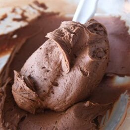 rubber spatula swirling chocolate frosting in glass bowl