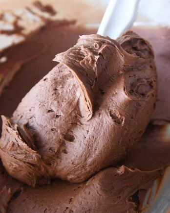 rubber spatula swirling chocolate frosting in glass bowl