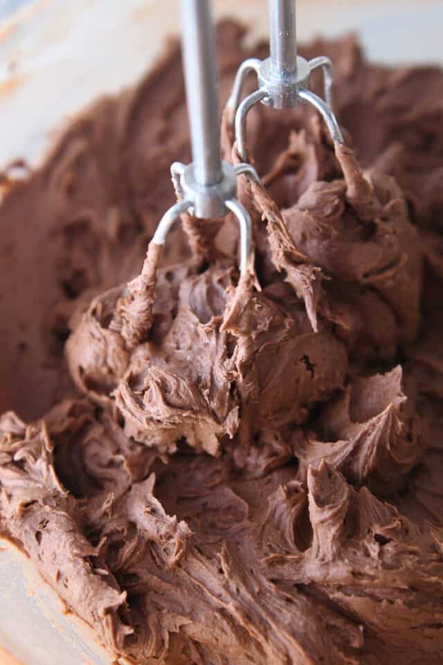 Mixing chocolate buttercream frosting in glass bowl with mixer.