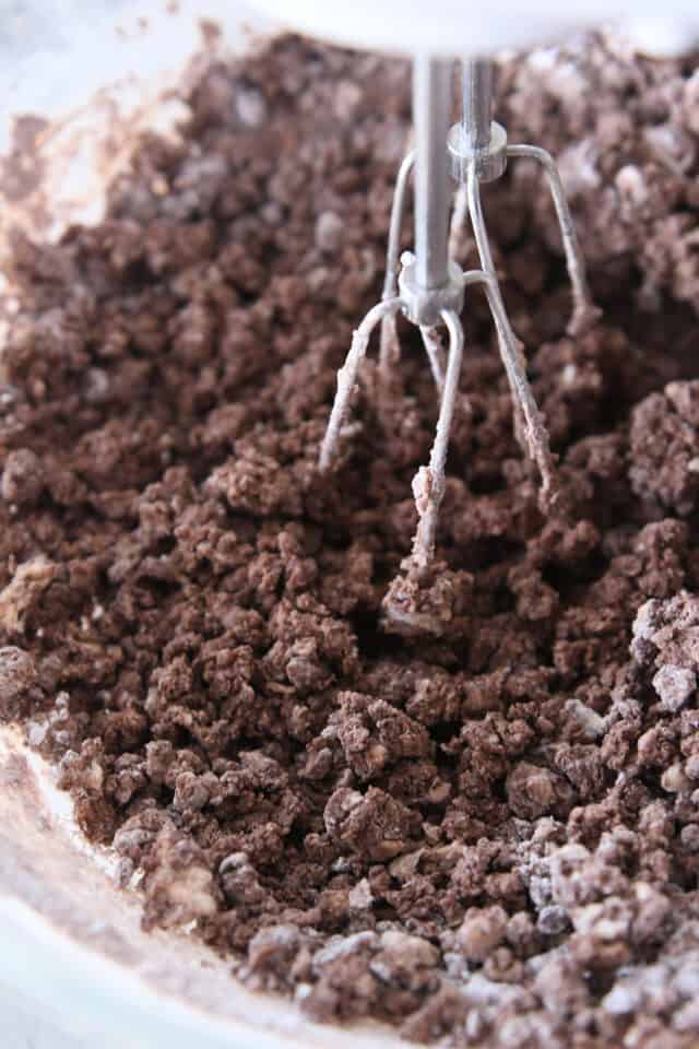 mixing dry ingredients into chocolate frosting with handheld electric mixer