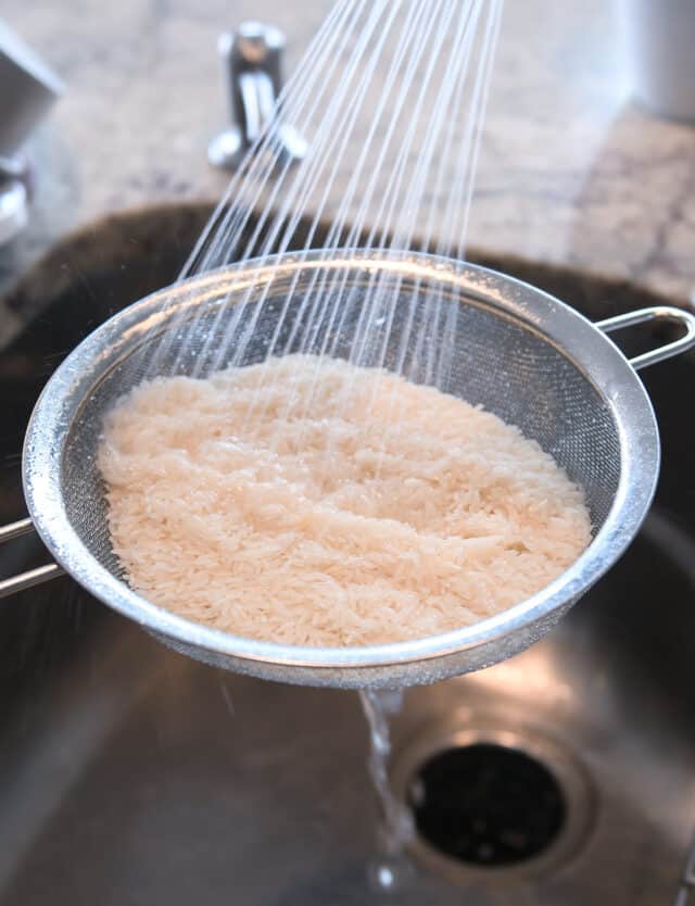 Rinsing rice in sink in metal colander.