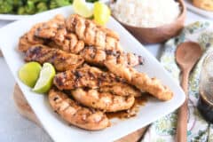 white platter with saucy, spiced chicken tenders and fresh lime wedges