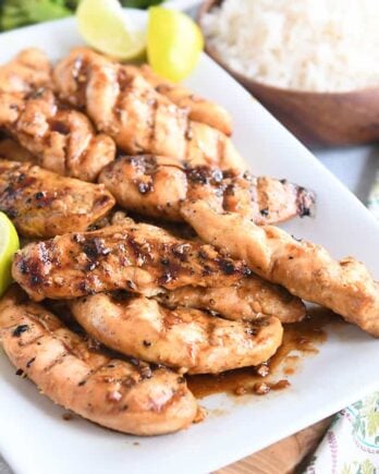 white platter with saucy, spiced chicken tenders and fresh lime wedges