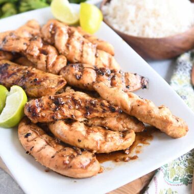 white platter with saucy, spiced chicken tenders and fresh lime wedges