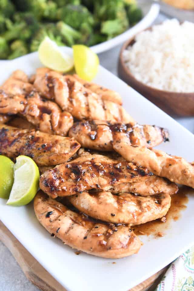 white platter with spiced chicken tenders and fresh lime wedges on wood board