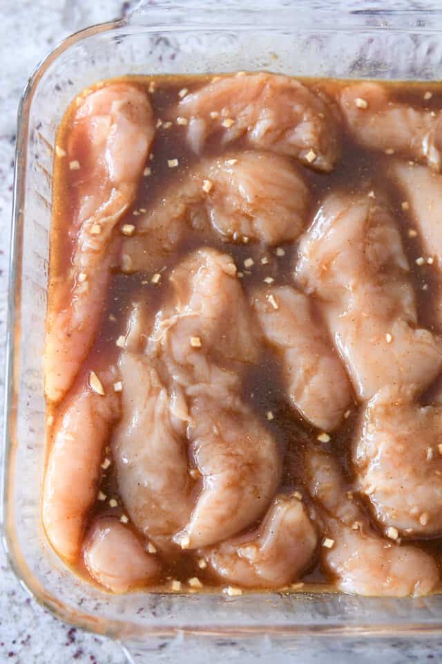 Raw chicken tenders in glass baking dish with marinade poured over the top.