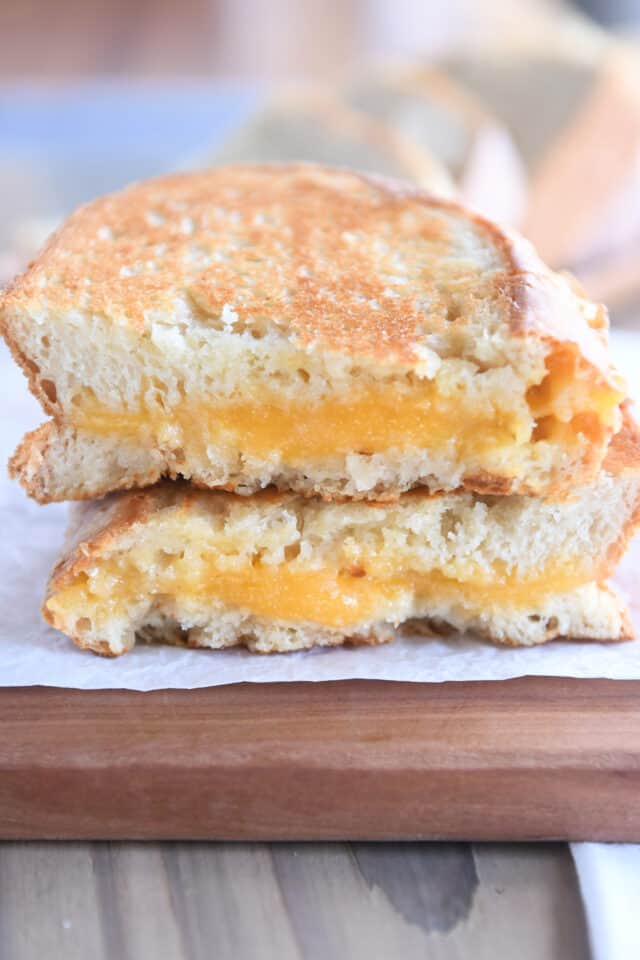 Two half slices of grilled cheese sandwich on wood cutting board.